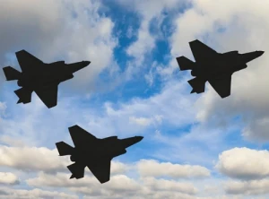 Three jet fighter planes in silhouette fly against a partly cloudy blue sky.
