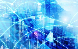 A city skyline with skyscrapers is overlaid by blue digital lines and glowing network nodes, symbolizing connectivity and modern technology.