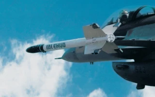 A close-up of a fighter jet in flight launching a white missile against a blue sky with some clouds.