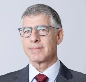 A middle-aged man with short gray hair and glasses, dressed as a vp of strategy in a dark suit, white shirt, and red tie, poses against a plain light background.