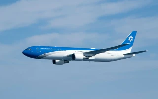 A blue and white passenger airplane from the Aviation Group flies against a partly cloudy sky. The aircraft features a Star of David symbol on the tail.