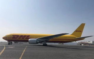 A large yellow DHL cargo airplane with red accents, possibly the result of passenger into cargo conversions, is taxiing on an airport runway under a clear sky. The DHL logo is visible on the side and tail of the aircraft.