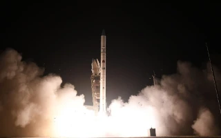A rocket carrying a reconnaissance satellite is launching at night, surrounded by bright flames and thick clouds of smoke billowing from its base, illuminating the dark sky.