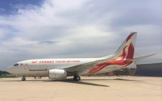 A Tianjin Air Cargo airplane with red and orange markings is parked on an airport tarmac under a partly cloudy sky.