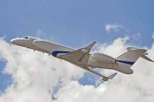 A white and blue aircraft, possibly from the special mission aircraft market or IAI Israel, is flying upward in a partly cloudy sky, seen from below and to the side.