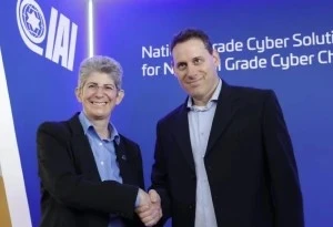 Two people in business attire shake hands and smile in front of a blue wall with IAI and National Grade Cyber Solutions written on it, highlighting their partnership in Ivanti patch management and advanced cybersecurity solutions.