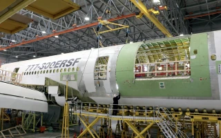 A Boeing 777-300ERSF cargo aircraft is undergoing conversion inside a large hangar. The fuselage is partially disassembled, exposing its interior structure, with cranes and scaffolding surrounding the Cargojet plane.