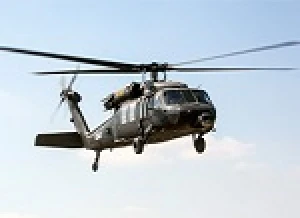 A black military helicopter equipped with an Odysight AI-based health monitoring system flies in the sky, its landing gears down and rotor blades spinning against a mostly clear light blue background.