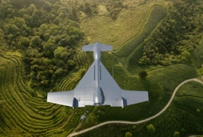 A grey drone flies over green, terraced fields and winding paths, surrounded by trees and vegetation.