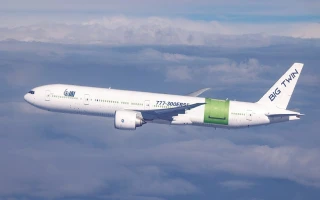 A white commercial airplane labeled BIG TWIN, possibly a 777, flies above the clouds. One engine is green, the other white. The mostly clear sky and distinctive livery hint at an IAI modification for FAA certification testing.