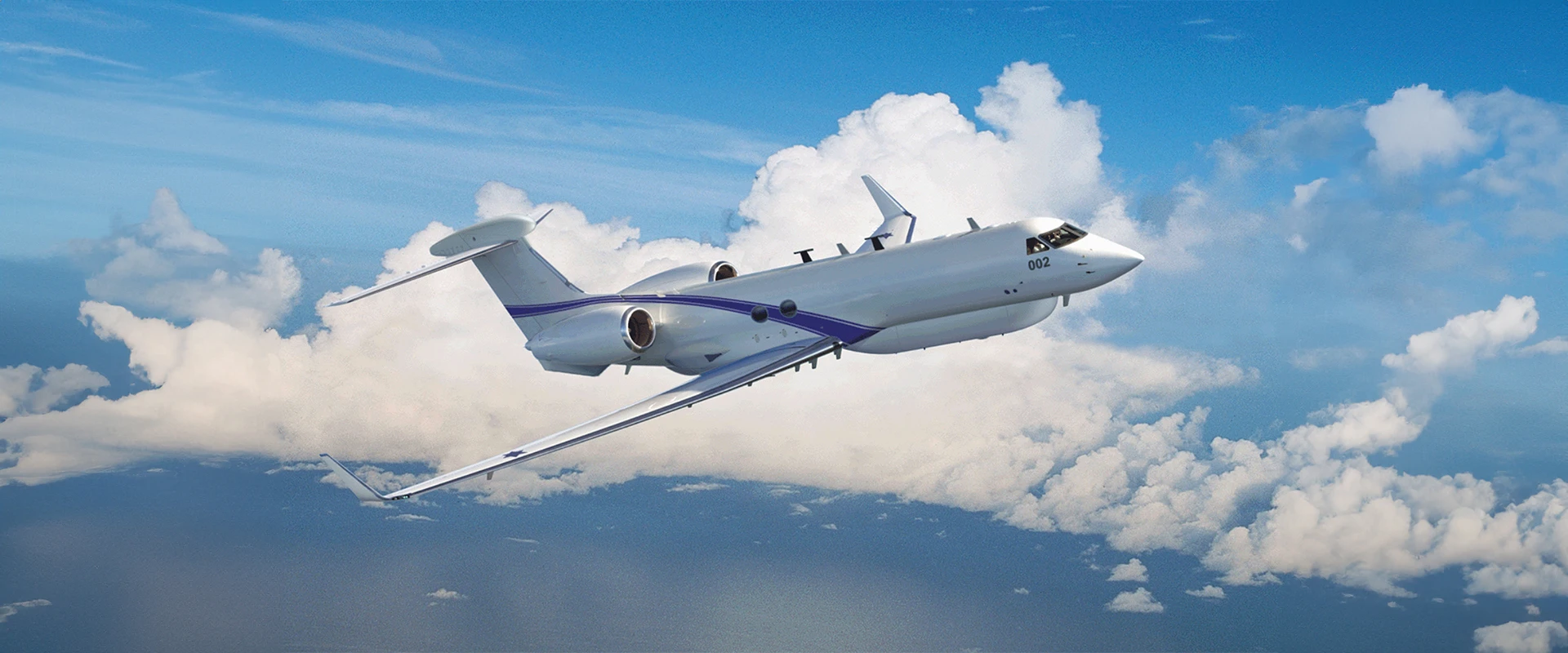 A white jet airplane with blue accents flies at an angle above clouds and a blue sky, equipped with a signal intelligence system, with the ocean visible below.
