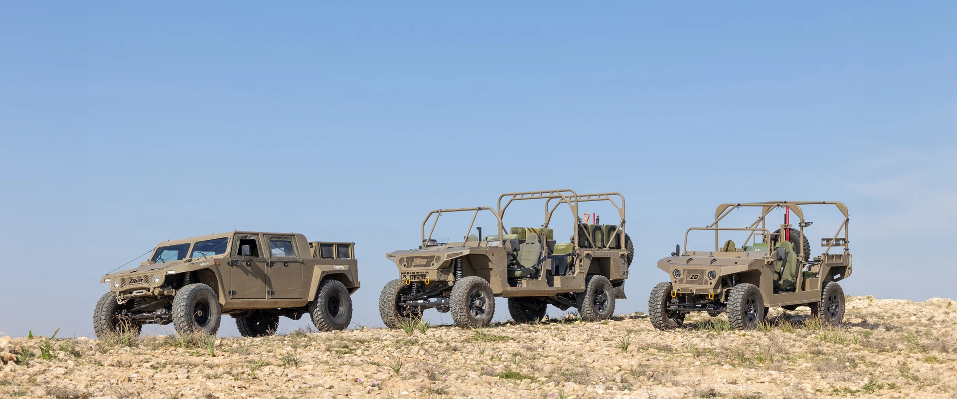 Three Z-Family military-style off-road vehicles in camouflage colors are parked on rocky terrain under a clear blue sky. Each vehicle features rugged tires and an open or semi-open frame design, ready for any adventure.