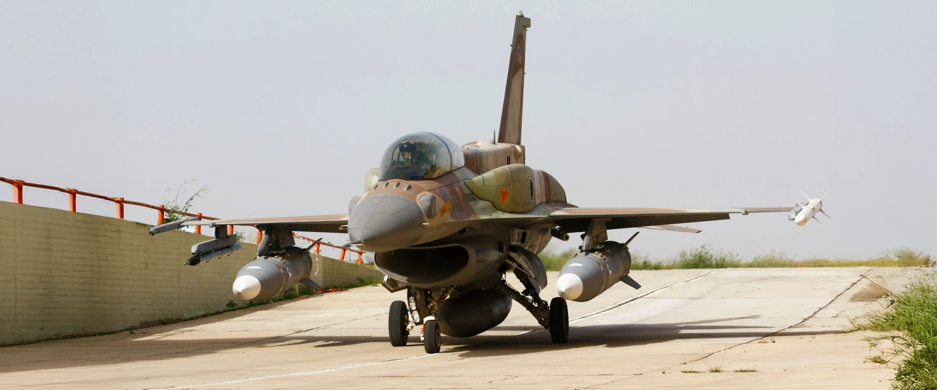 A military fighter jet with camouflage paint is taxiing on a concrete runway, loaded with missiles—ready to intercept any launched ballistic missile—against a clear sky.