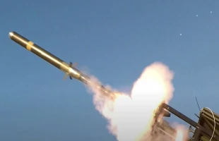 A laser designated missile launches from its platform, trailing flames and smoke against a clear blue sky.
