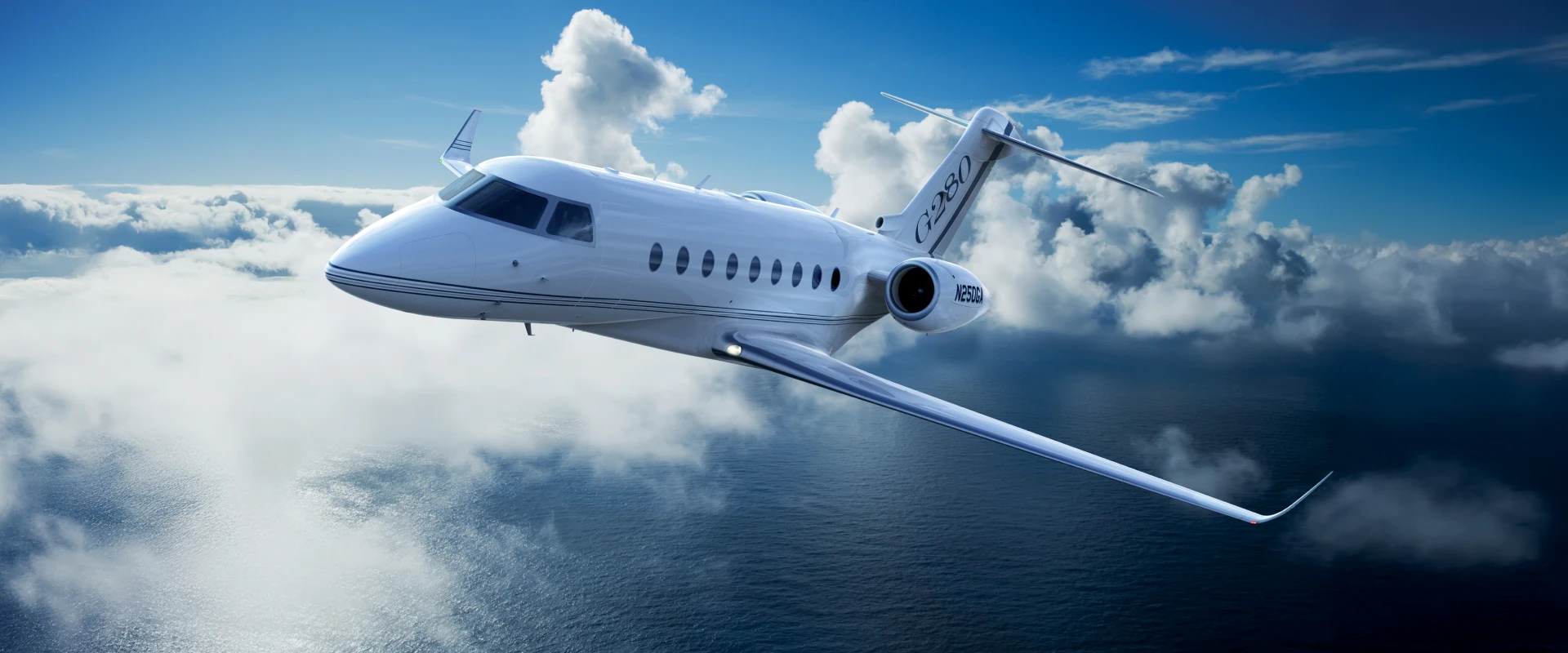 A sleek white business jet soars above the clouds over an ocean, with clear blue sky and sunlight illuminating the stunning scene.