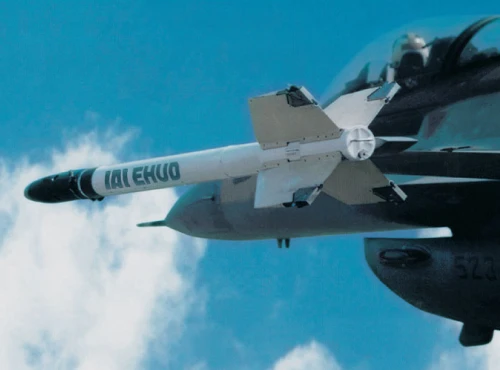 A close-up view of a white missile labeled TAI EHKU, part of a combat training system, mounted on the wing of a fighter jet against a blue sky with scattered clouds.