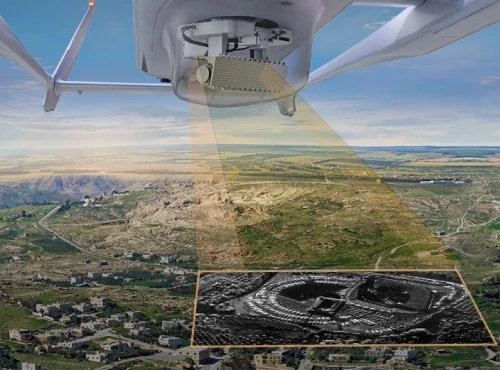 An aerial view of a landscape is captured from an aircraft equipped with a GMTI radar system, which scans the ground below and displays a detailed black-and-white radar image of the terrain.