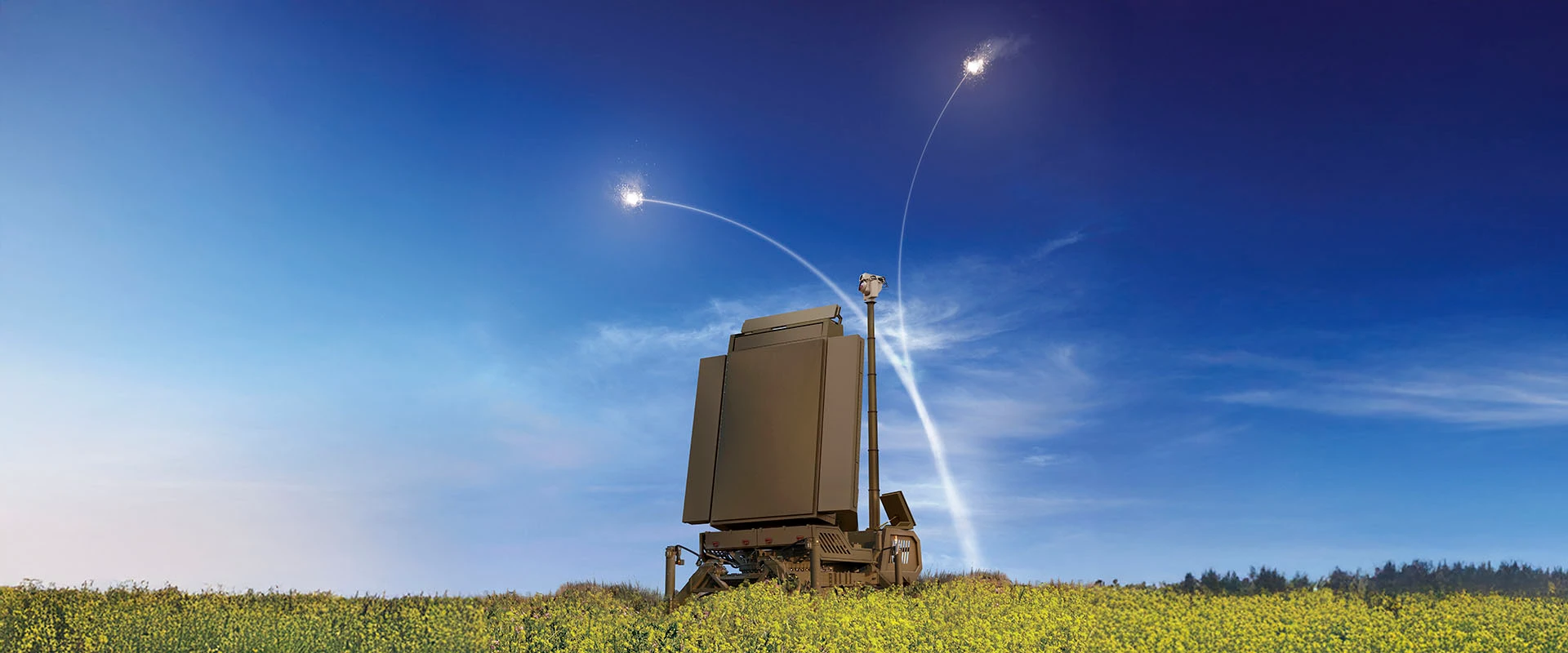 A military mmr radar system sits in a grassy field under a blue sky, launching two defensive interceptor missiles that leave white trails arcing upward against the backdrop of clouds.