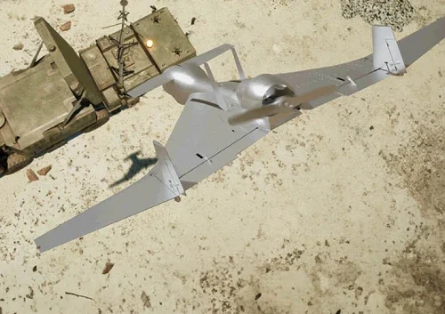 A silver military drone with twin propellers and a wide wingspan, equipped with a fire-and-forget missile, is parked on sandy ground next to a green military vehicle viewed from above.