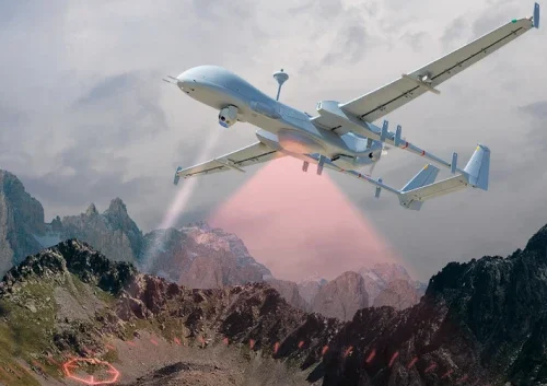 A long endurance UAV flies over rugged mountains, emitting red scanning beams toward the ground, illuminating a circular target area among the rocky terrain under a cloudy sky.