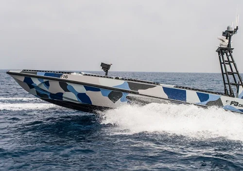 A modern speedboat vessel with a blue, gray, and white camouflage pattern glides quickly over the ocean, creating a spray of water under a cloudy sky—showcasing the agility of an advanced USV system.