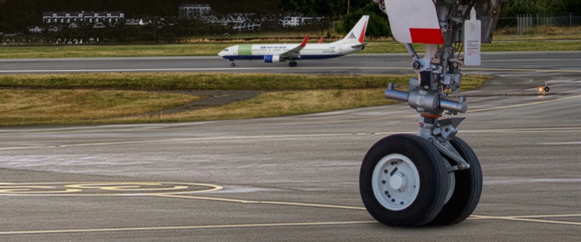 The image shows the front landing gear of an airplane on an airport taxiway, highlighting the importance of Landing Gear MRO, with another airplane taxiing in the background on a parallel runway. Grass and trees border the airfield.