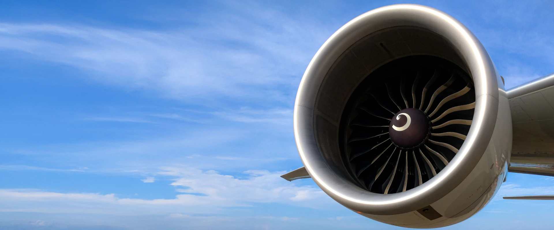 Close-up of a jet engine, available for lease & exchange, attached to an airplane wing against a bright blue sky with scattered clouds in the background.
