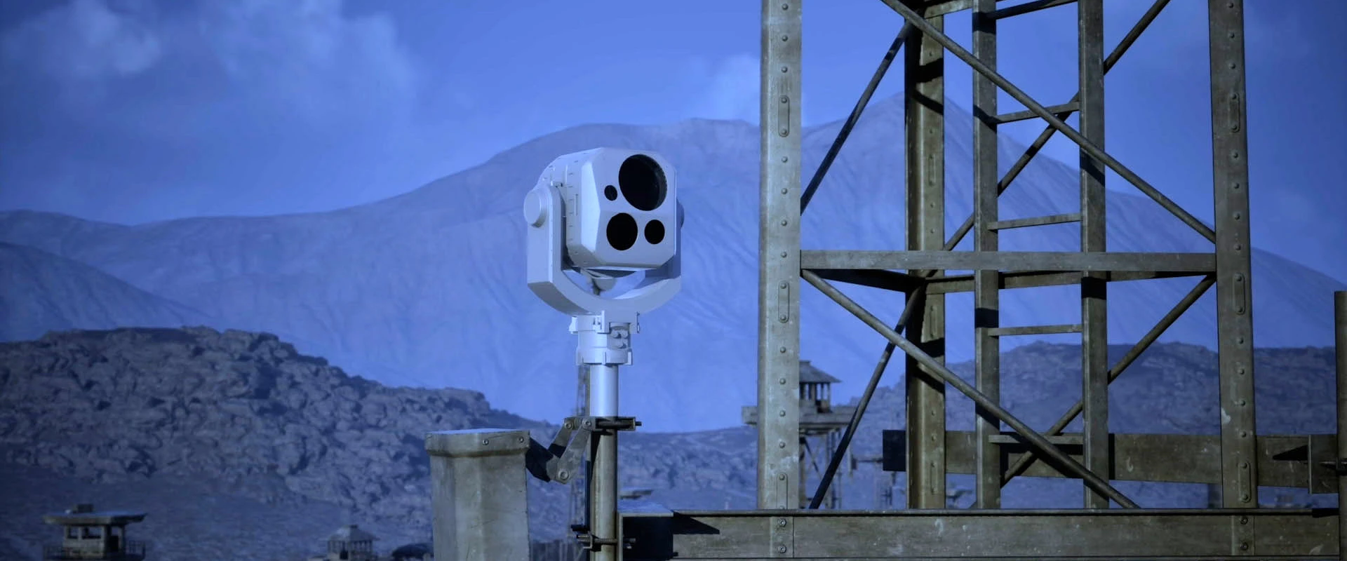 A spectral EO system with multiple lenses is mounted on a pole near a metal structure, set against a mountainous, rocky landscape under a blue sky.