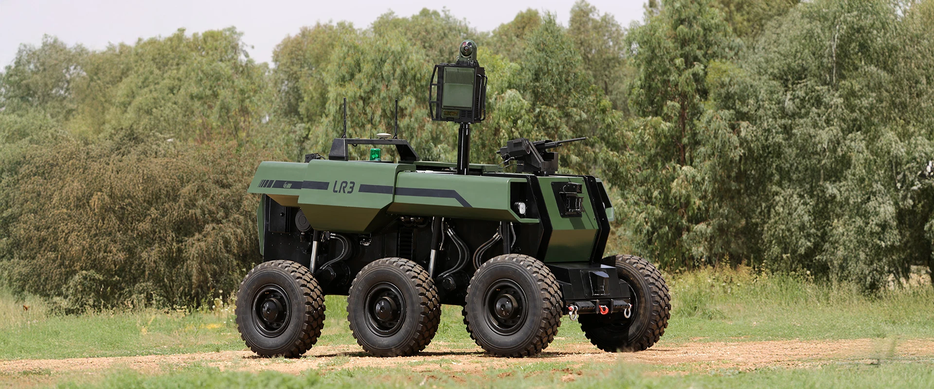 A green, six-wheeled unmanned ground vehicle equipped with cameras and sensors operates as an autonomous combat system on grassy terrain, with trees in the background.