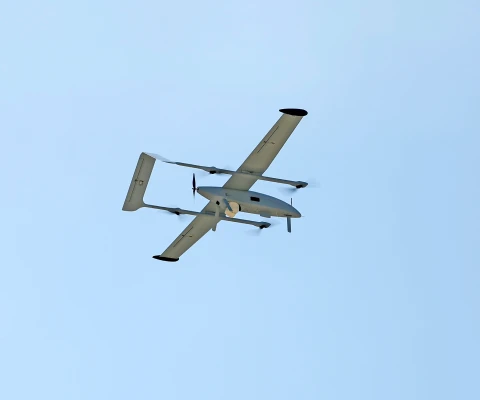 A fixed-wing drone and multi-copter UAV with two propellers is flying in a clear blue sky, seen from below.