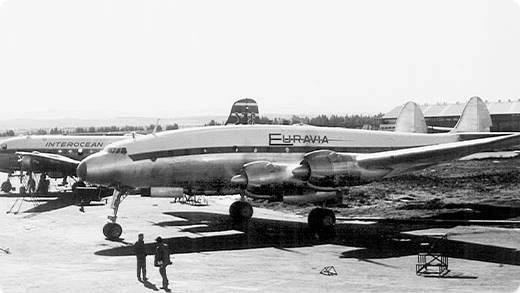 Black and white photo of a vintage Euravia passenger airplane parked on an airfield, with another Interocean aircraft nearby and people walking on the tarmac.