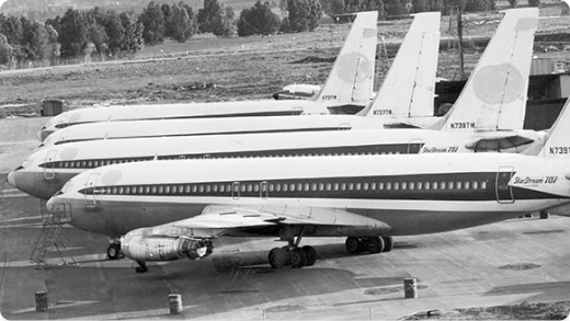 Four vintage commercial airplanes are parked side by side on an airport tarmac, with their tails aligned. The planes have Skydream 701 markings and trees can be seen in the background.
