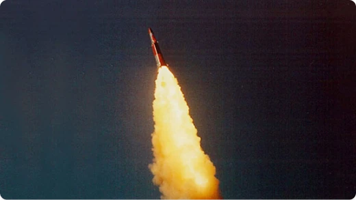 A rocket launches into the dark sky, leaving behind a bright, fiery trail of exhaust and smoke.