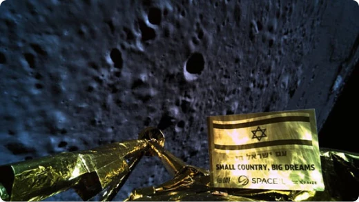 Gold foil from a spacecraft with an Israeli flag and the words Small Country, Big Dreams in English and Hebrew, set against the cratered surface of the Moon in the background.