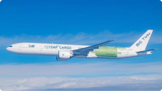 A large white airplane with AERCAP CARGO and BIG TWIN written on the side flies in a blue sky. Part of the fuselage near the aft section is painted green.