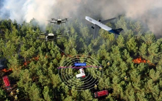 Aerial view of a forest fire with drones, a plane flying overhead, firefighters on the ground, and fire trucks near the burning trees. Digital graphics show signal waves from a device monitoring the scene, as seen in the iai annual report.