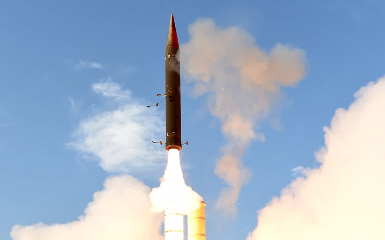 An anti ballistic missile launches vertically into the sky, surrounded by smoke and flames, soaring against a clear blue background.