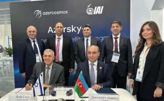 Seven people in business attire pose for a photo at a formal event table with Israeli and Azerbaijani flags, under banners for Azercosmos and IAI. Two men are seated while five stand behind them, all smiling.