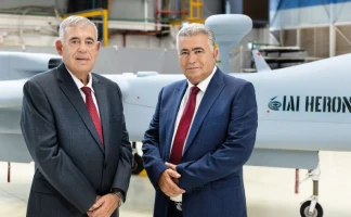 Two men in suits stand before a large unmanned aerial vehicle labeled IAI HERON inside an industrial facility, a scene often featured in the Israel Aerospace Industries annual report.