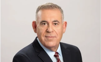 A middle-aged man with short gray hair, wearing a dark suit, light blue shirt, and striped tie, poses confidently against a plain light background, reminiscent of an executive at the XPRIZE Wildfire Competition.