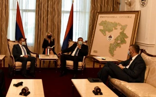 Four people in formal attire and face masks sit in an office with two flags and a large map labeled PREDSEDNIK REPUBLIKE behind them, appearing to discuss topics related to the online cyber academy.