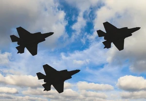 Three stealth fighter aircraft silhouetted against a partly cloudy blue sky, flying in precise formation.