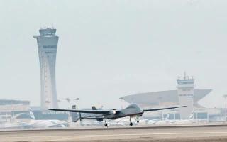 A drone is taking off from an airport runway, with several airplanes and two large airport control towers visible in the background, showcasing a bustling scene of UAV landing and departures.