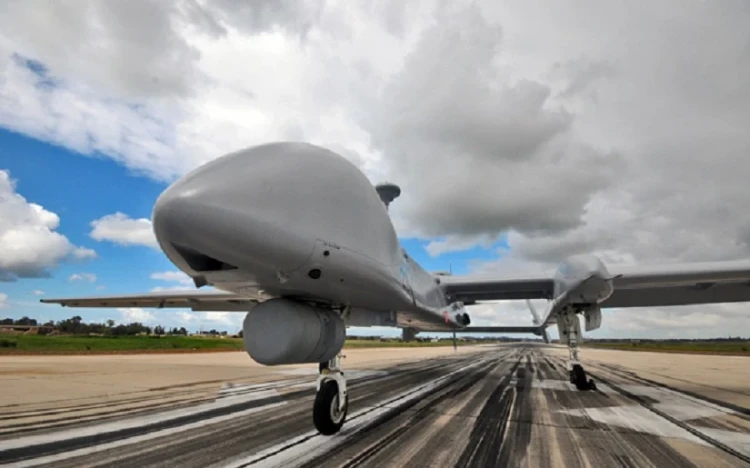 A large IAI unmanned aerial vehicle (UAV) with a gray body and landing gear is positioned on a runway under a partly cloudy sky. The low, close angle accentuates its size and intelligence-gathering features.