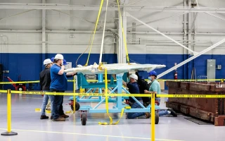 Several workers in hard hats and safety vests assemble or inspect a large, light blue B767-300 aircraft component at Bedek Aviation’s industrial facility, surrounded by yellow caution tape and tools during conversion operations.