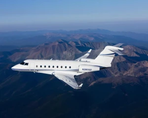 A white private jet with blue stripes, engaged in civil aviation activities, is flying above a mountainous landscape under a clear sky.