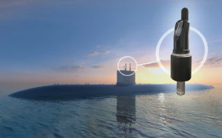 A submarine is partially submerged in calm water at sunset, with a large sensor or probe digitally superimposed over its sail, highlighted by a glowing circle.