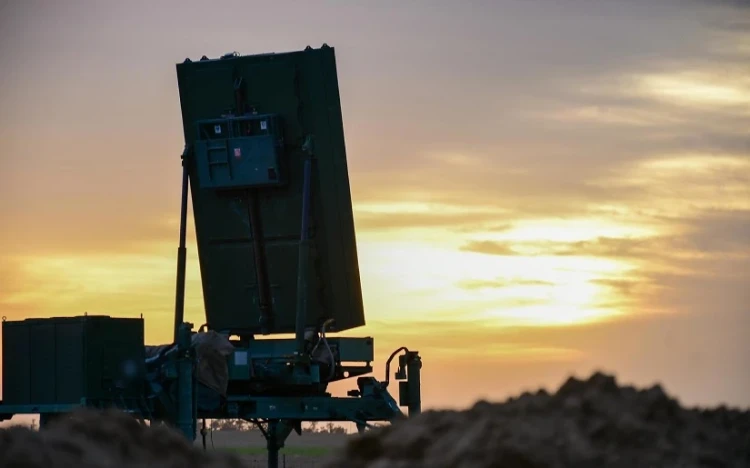 A large MMR military radar system is positioned outdoors, silhouetted against a dramatic sunset sky, with a pile of dirt in the foreground—a testament to cutting-edge defence against swarm threats.
