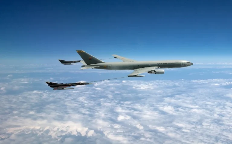 An IAI military aircraft refuels a fighter jet mid-air using a hose and drogue system, soaring high above the clouds with a clear blue sky in the background.