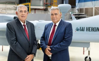 Two men in suits and red ties stand in front of a large gray drone labeled IAI HERON inside an industrial facility, reflecting the innovation highlighted in the Israel Aerospace Industries annual report.